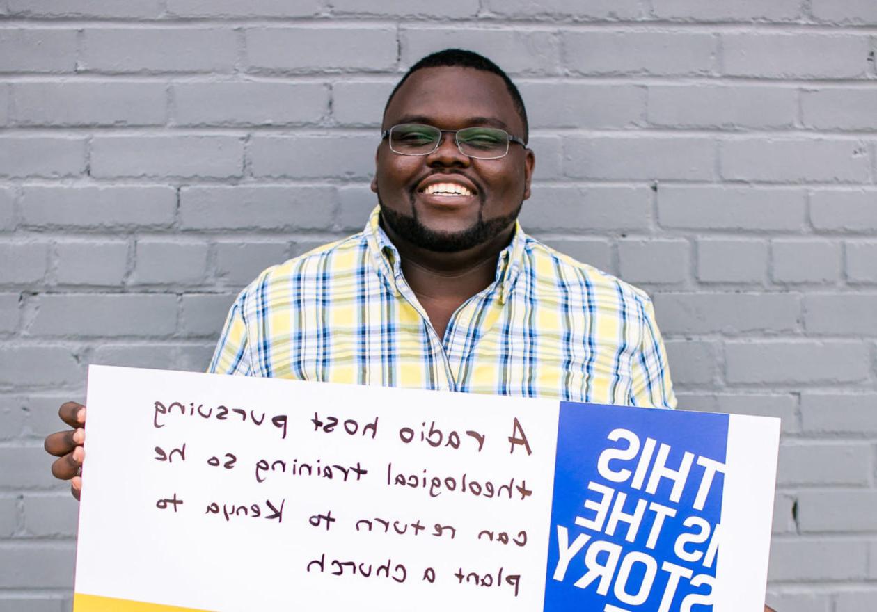 A smiling graduate student holding a sign that reads, "This is the story of a radio host pursuing theological training so he can return to Kenya to plant a church."